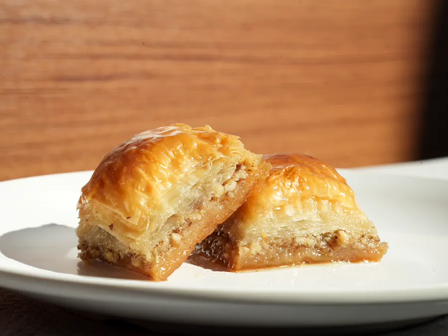 Zwei Baklava-Stücke mit vielen Lagen Teig auf einem weißen Teller