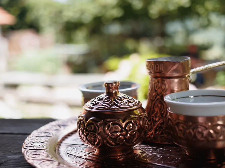 Kupfernes Kaffeeset mit Džezva, Zuckerdose und Fildžan auf einem Tisch im Garten