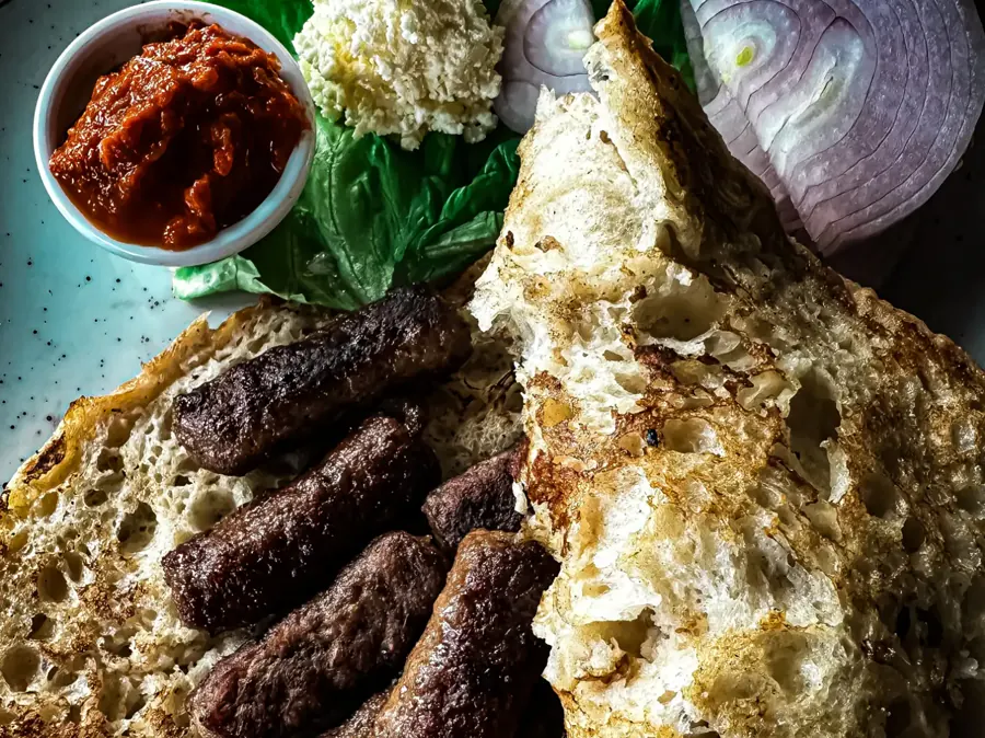 Ćevapi in Lepinja mit Zwiebeln und Kajmak auf einem Metallteller